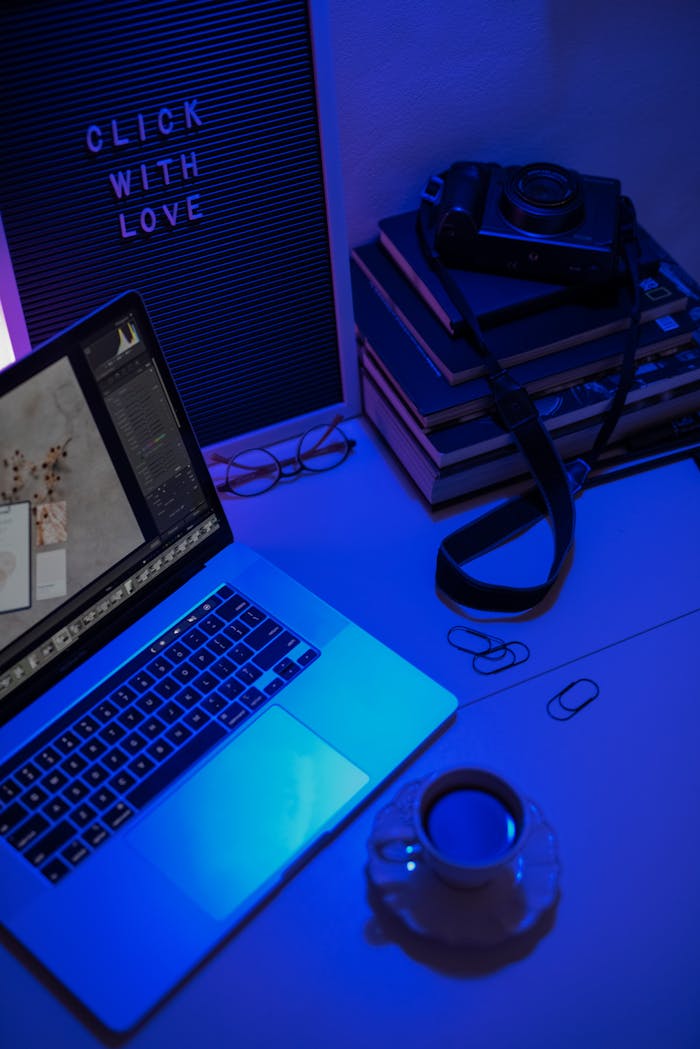 A stylish workspace featuring a laptop, camera, and coffee under dramatic lighting.